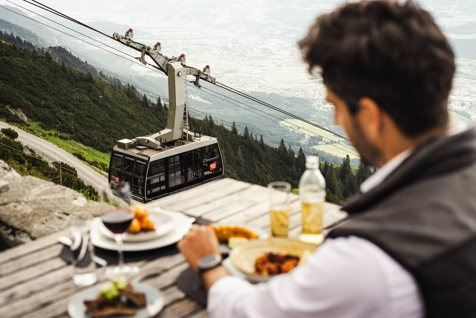Mann beim Essen am Berg, im Hintergrund sieht man die Nordkettenbahn.